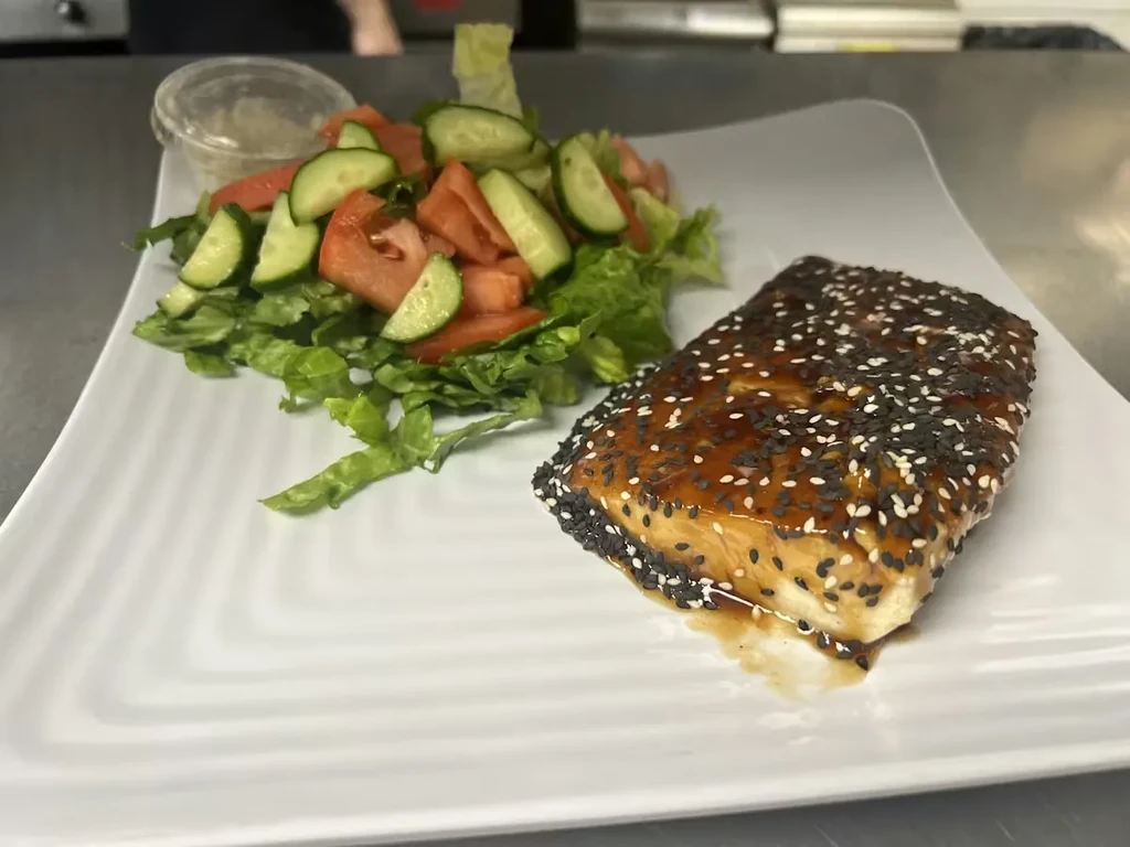 Glazed salmon with sesame seeds and side salad on a square plate.