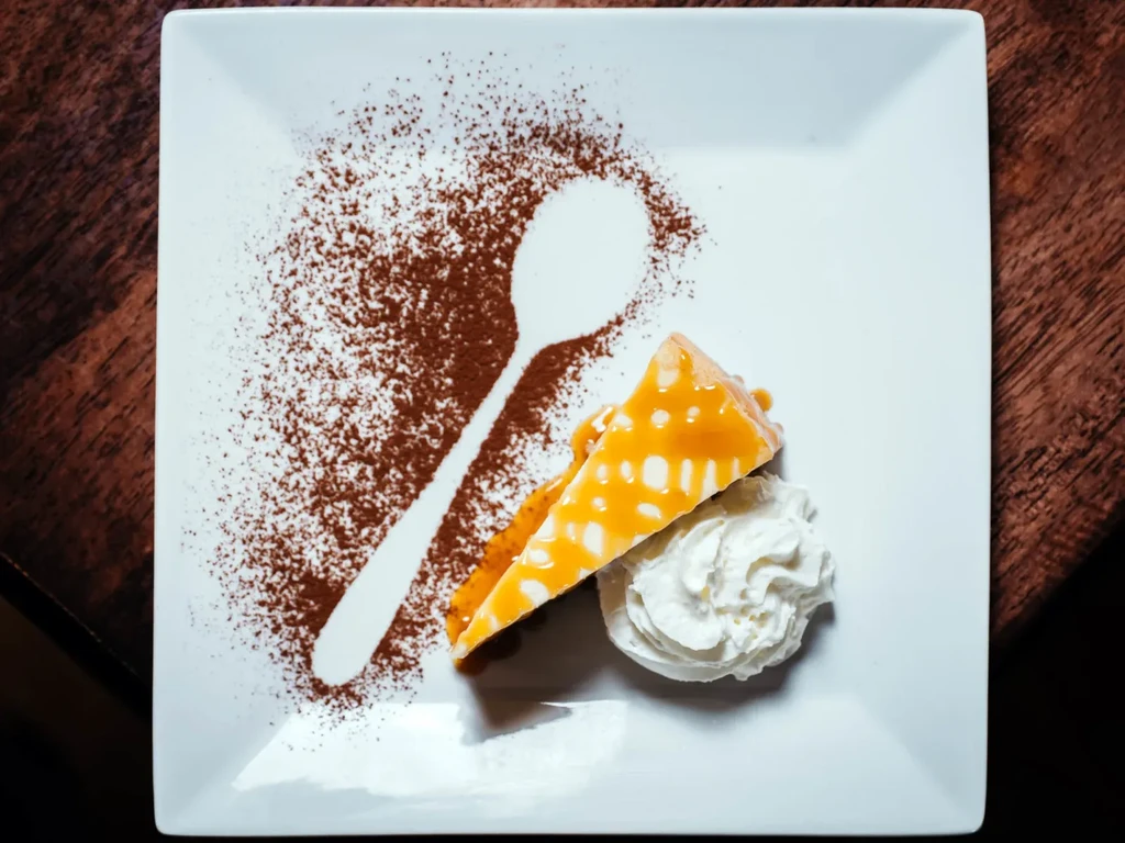Light dessert slice with caramel, whipped cream, cocoa spoon silhouette.