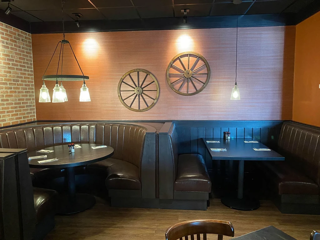 Rustic restaurant interior with dark leather booths and wagon wheel decor.