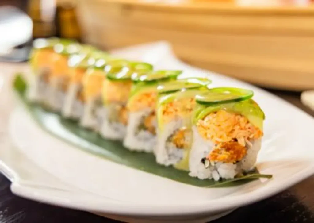Nine sushi rolls with orange topping and green cucumber.