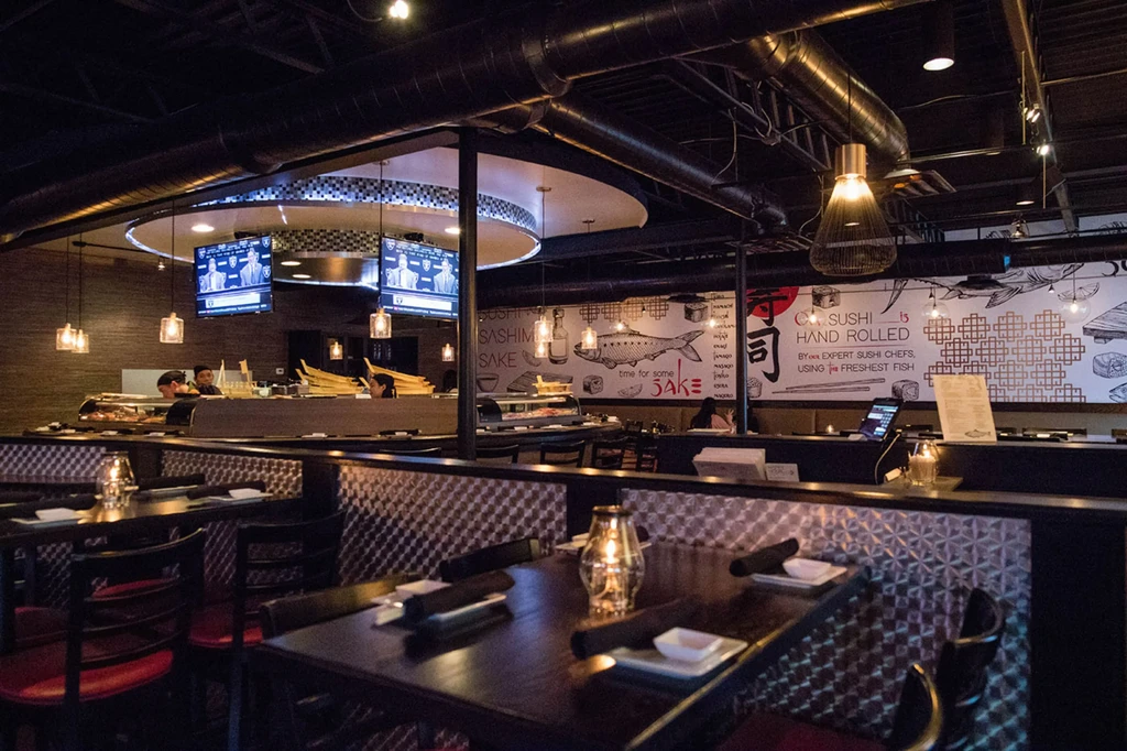 Dark, modern sushi restaurant interior with sushi bar and dining tables.