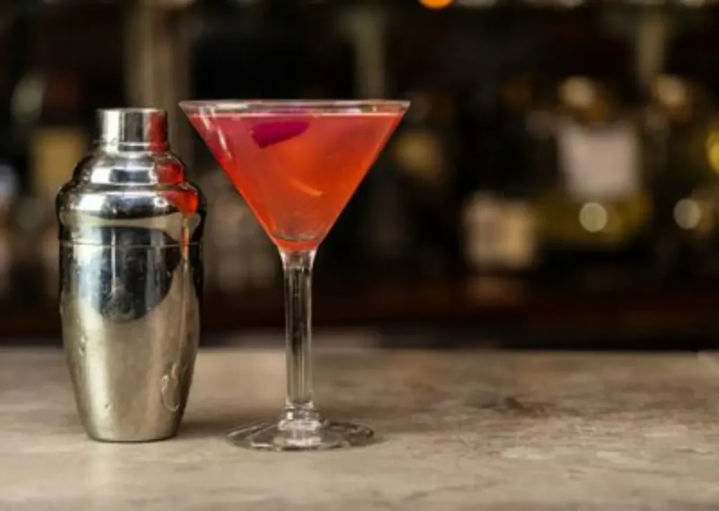 Polished silver shaker and pink garnished martini on a dim bar.