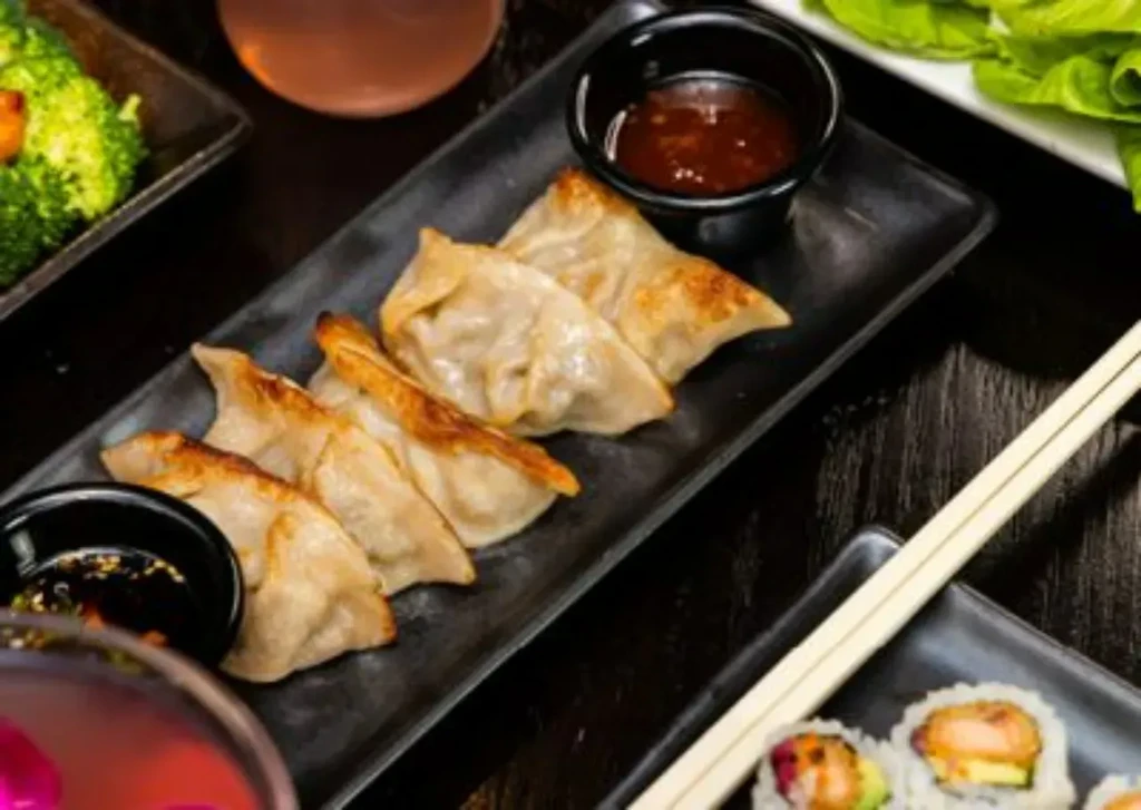 Overhead close-up of Asian dumplings, sushi, and broccoli on dark table.