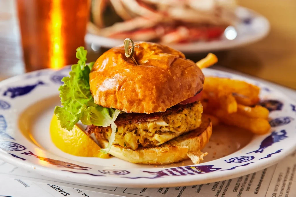 Seafood burger, fries, lemon, on a marine-decorated plate.