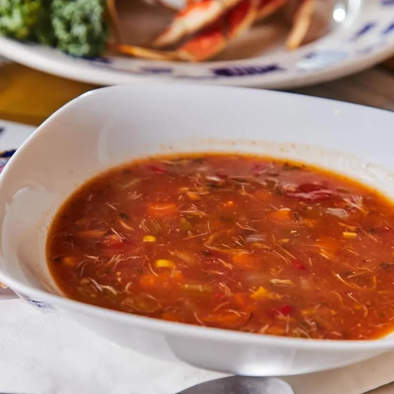 White bowl of hearty reddish-orange soup with meat, corn, carrots.