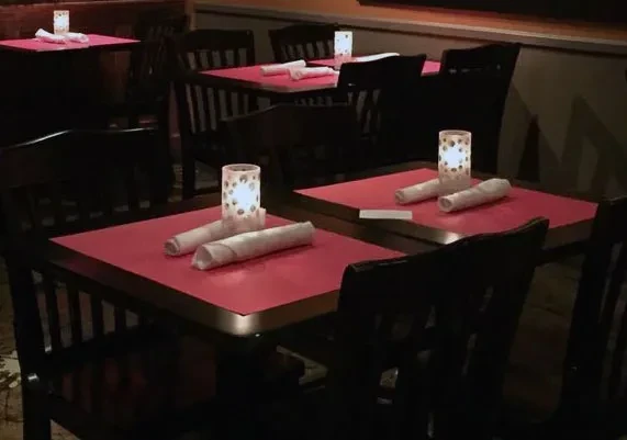 Set restaurant tables with red placemats, dark chairs, and warm candlelight.