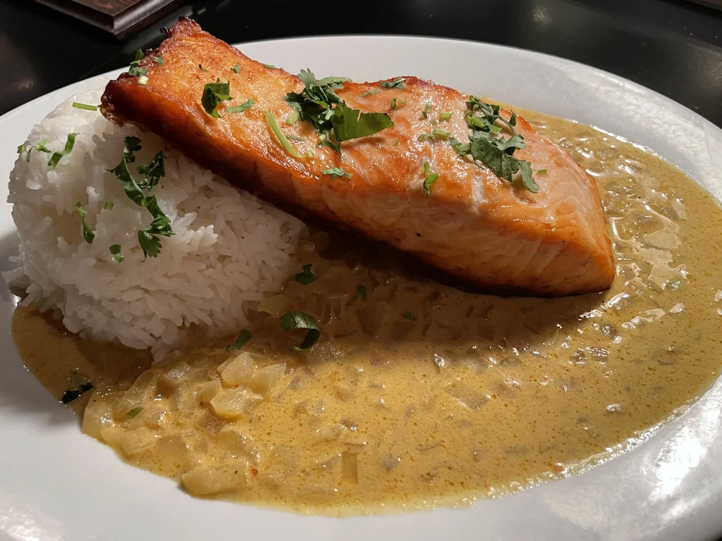 Plated golden-brown salmon, white rice, chunky sauce, and herbs.