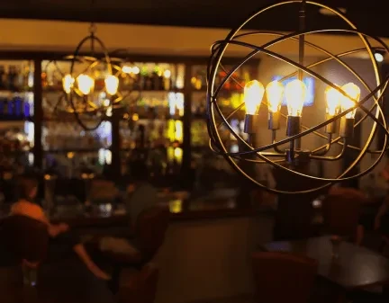 Close-up modern chandelier with glowing Edison bulbs, blurred bar background.