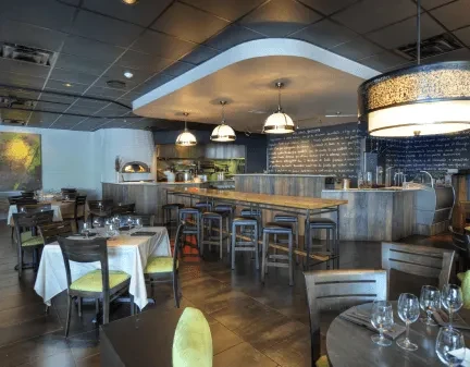 Modern restaurant interior with dining tables, communal table, bar, open kitchen.