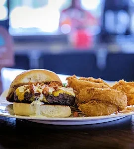 Close-up of gourmet burger with melted cheese, bacon, and crispy onion rings.
