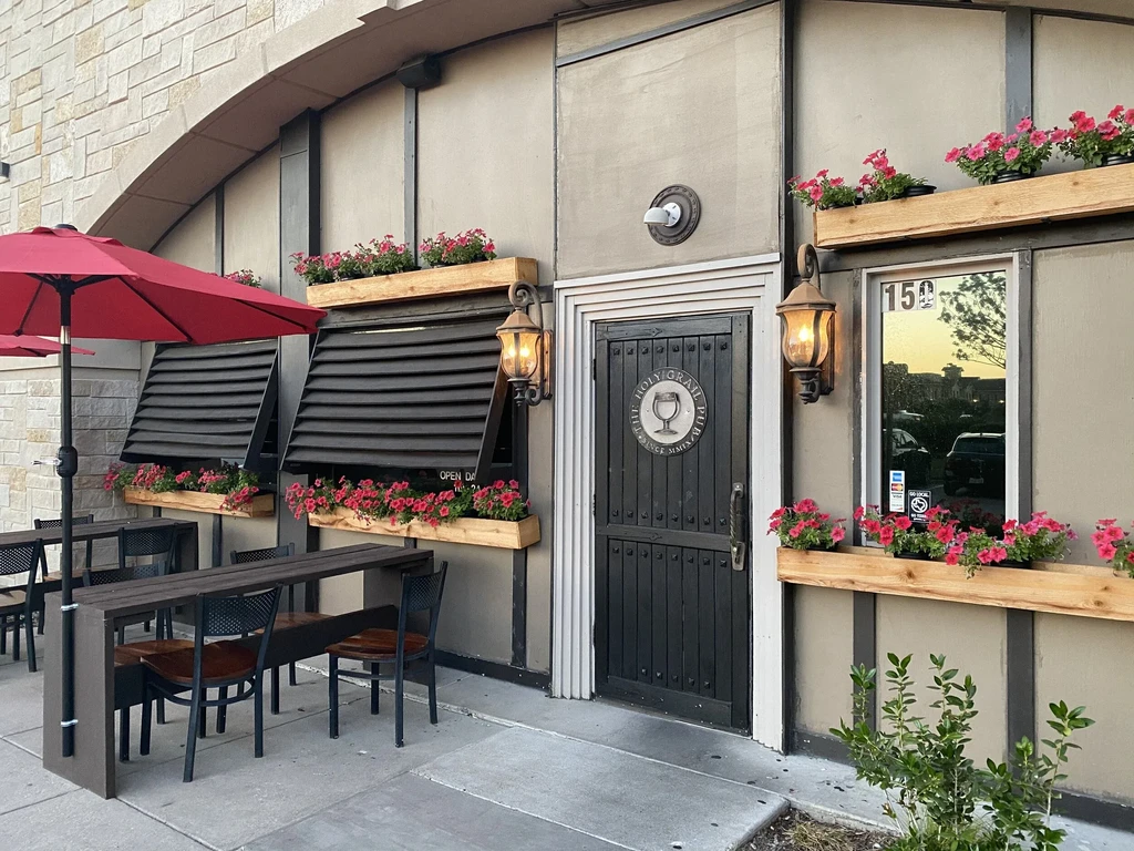Exterior of The Holy Grail Pub, stone facade, outdoor dining, pink petunias.