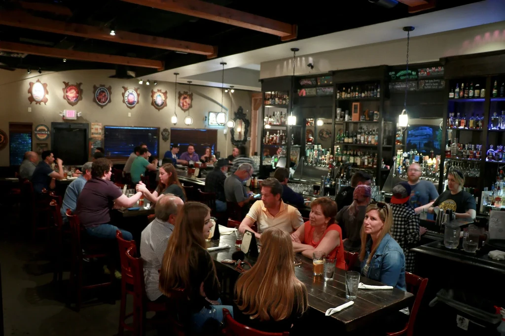 Lively pub interior with patrons, a long bar, and rustic decor.