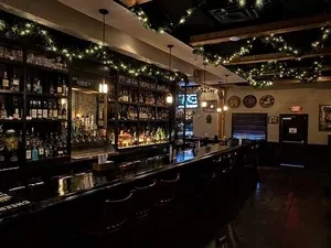 Dimly lit bar with polished counter, backlit liquor bottles, string lights.