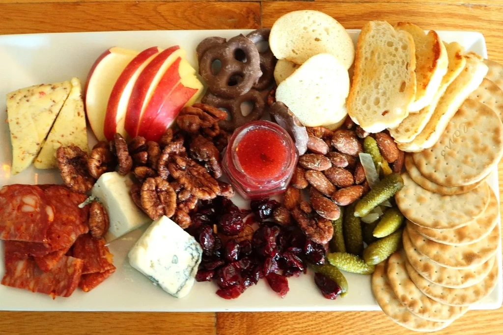 Charcuterie board with various cheeses, meats, fruits, nuts, crackers, and jam.