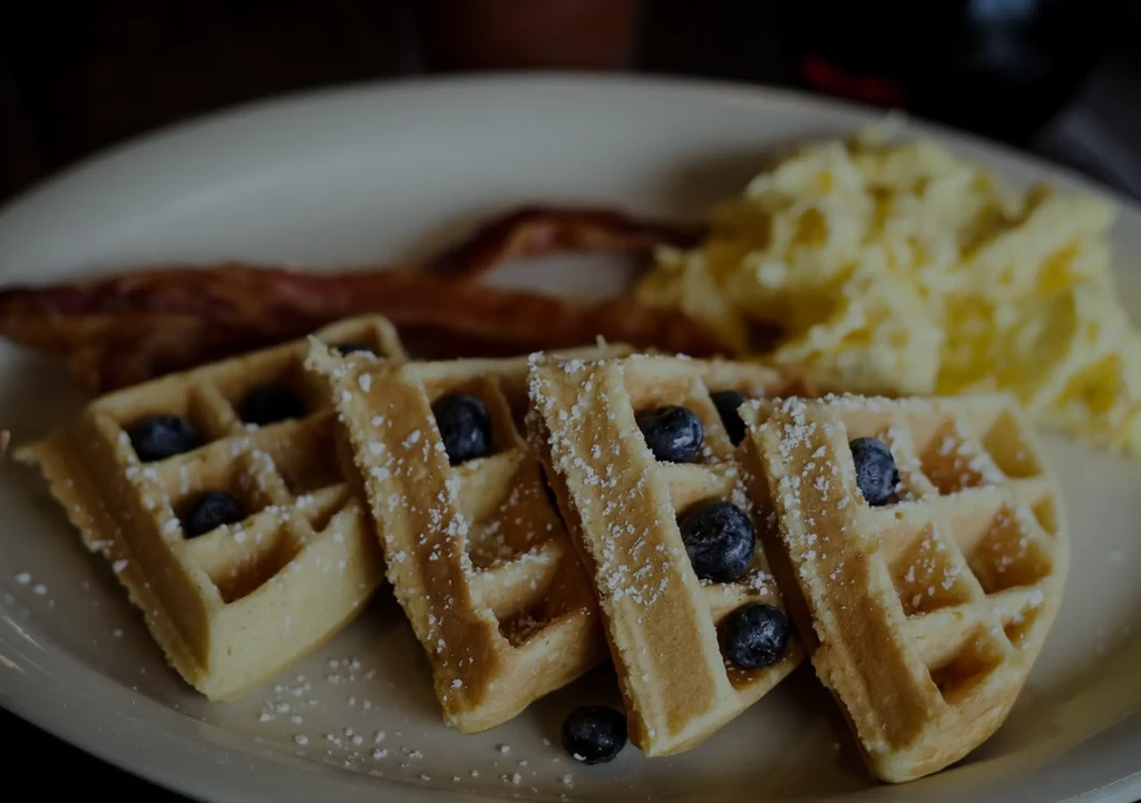 Breakfast plate with waffles, blueberries, scrambled eggs, and crispy bacon.