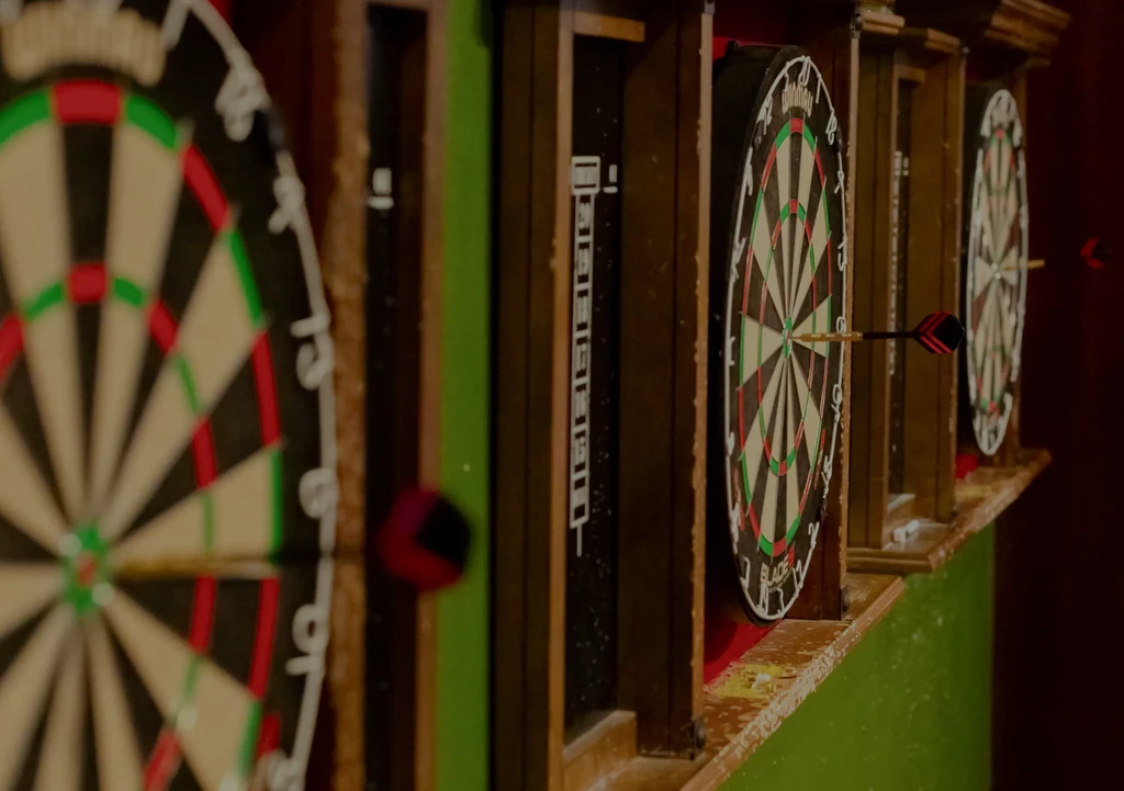 Dart in bullseye on middle dartboard in a dimly lit pub.