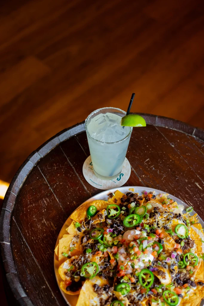 Loaded nachos and a margarita on a rustic wooden table.
