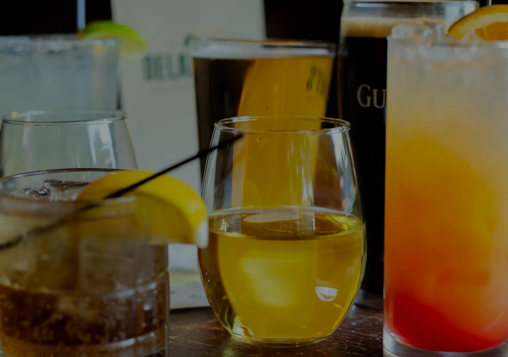 Variety of alcoholic drinks on a wooden table, some blurred in background.