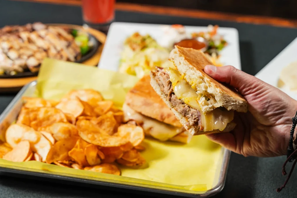 Hand holding a golden-brown pressed sandwich, showing its cross-section and chips.