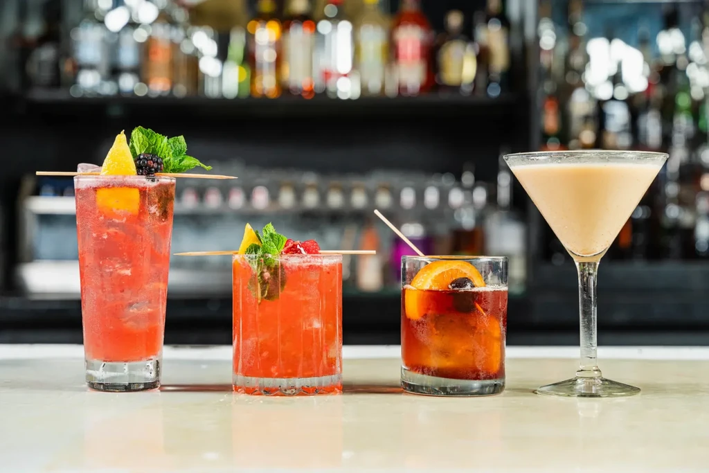 Four colorful cocktails on a bar counter, with a blurred bar.
