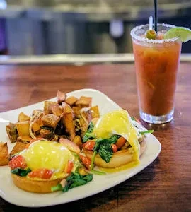 Plate of Eggs Benedict, crispy potatoes, and a garnished Bloody Mary.