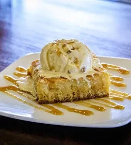 Golden cake topped with vanilla ice cream and caramel on a white plate.