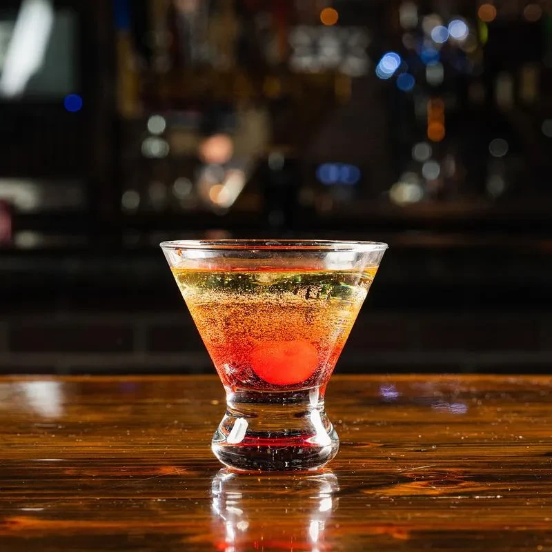 Layered cocktail in a martini glass with a cherry on a wooden bar.