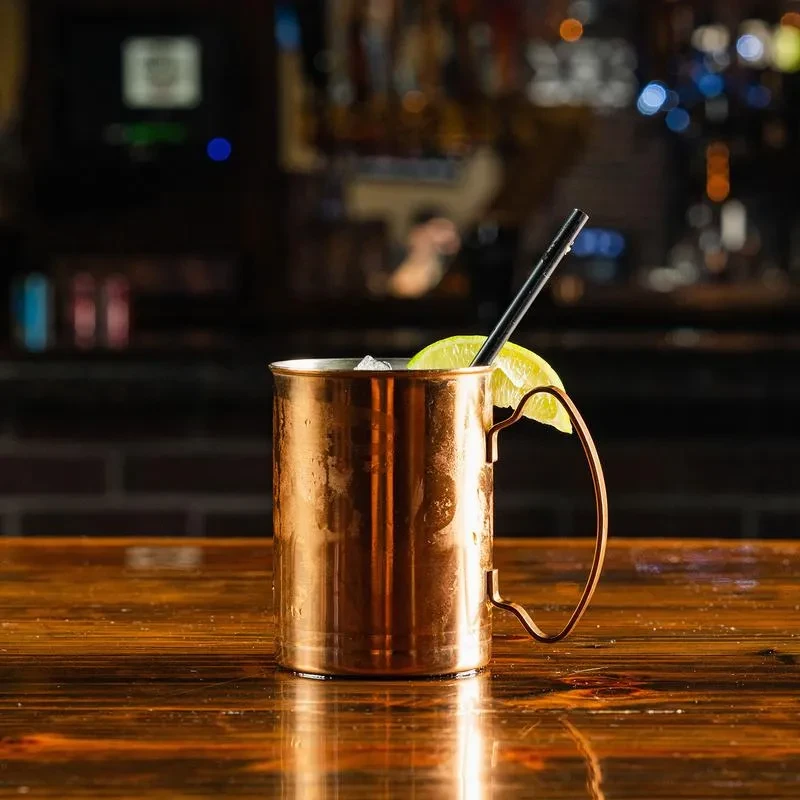 Copper Moscow Mule mug, chilled with lime, on a wooden bar.