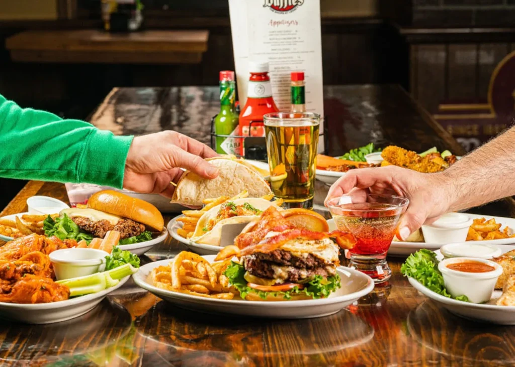 Hands reaching for burgers, wings, tacos, and drinks at Duffy's.