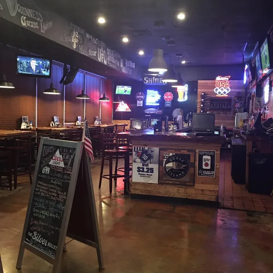 Dimly lit sports bar interior with TVs, bar, and colorful neon signs.