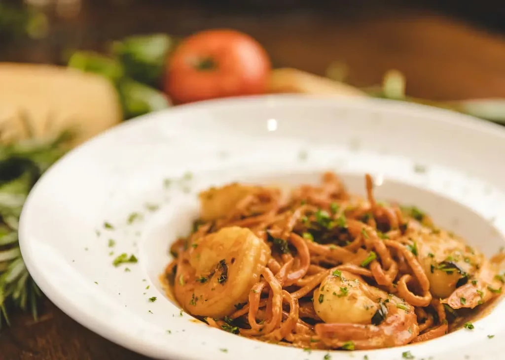 Creamy pasta with shrimp and red sauce, garnished with green herbs.
