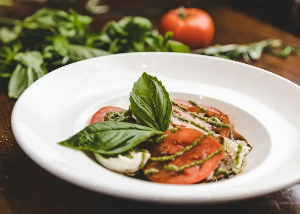 Plated Caprese salad with tomatoes, mozzarella, basil, and pesto.