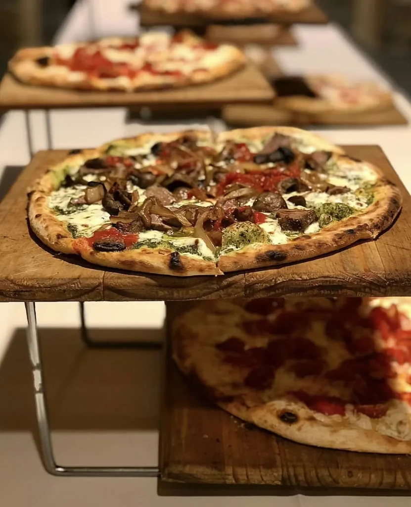 Multiple pizzas on wooden boards, main pizza topped with pesto and cheese.