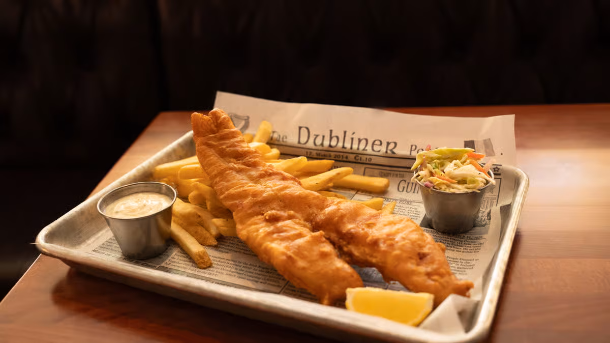 Fish and chips with dipping sauce and coleslaw on newspaper.