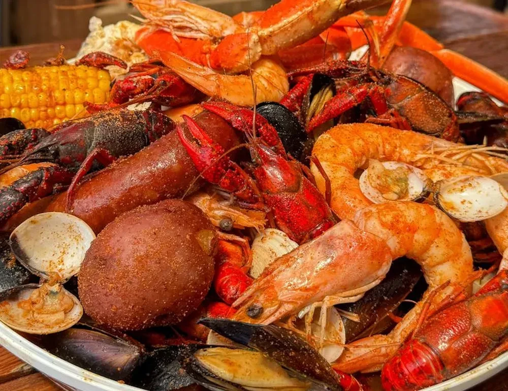 Platter overflowing with seasoned crawfish, shrimp, crab legs, corn, and potatoes.