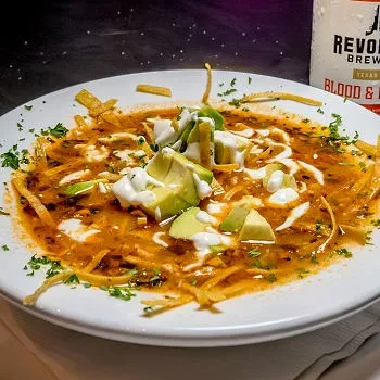 Hearty reddish-brown soup with avocado, sour cream, and crispy tortilla strips.