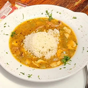 Close-up: white bowl of gumbo with rice, shrimp, and vegetables.