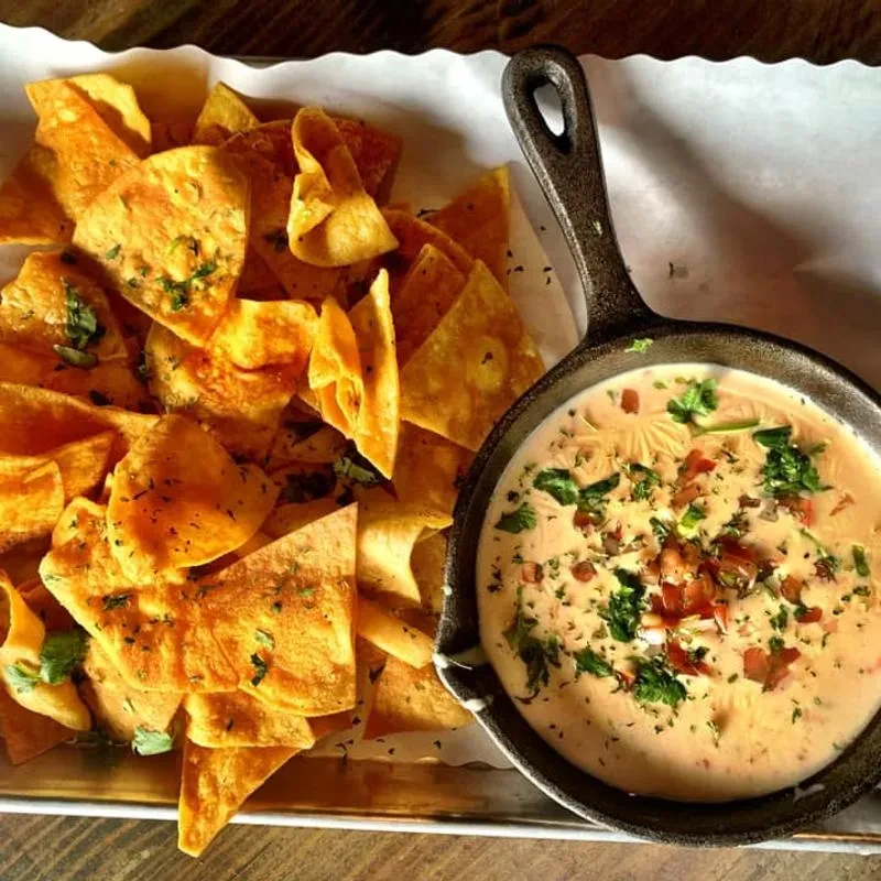 Golden tortilla chips and queso in a skillet with cilantro and tomatoes.