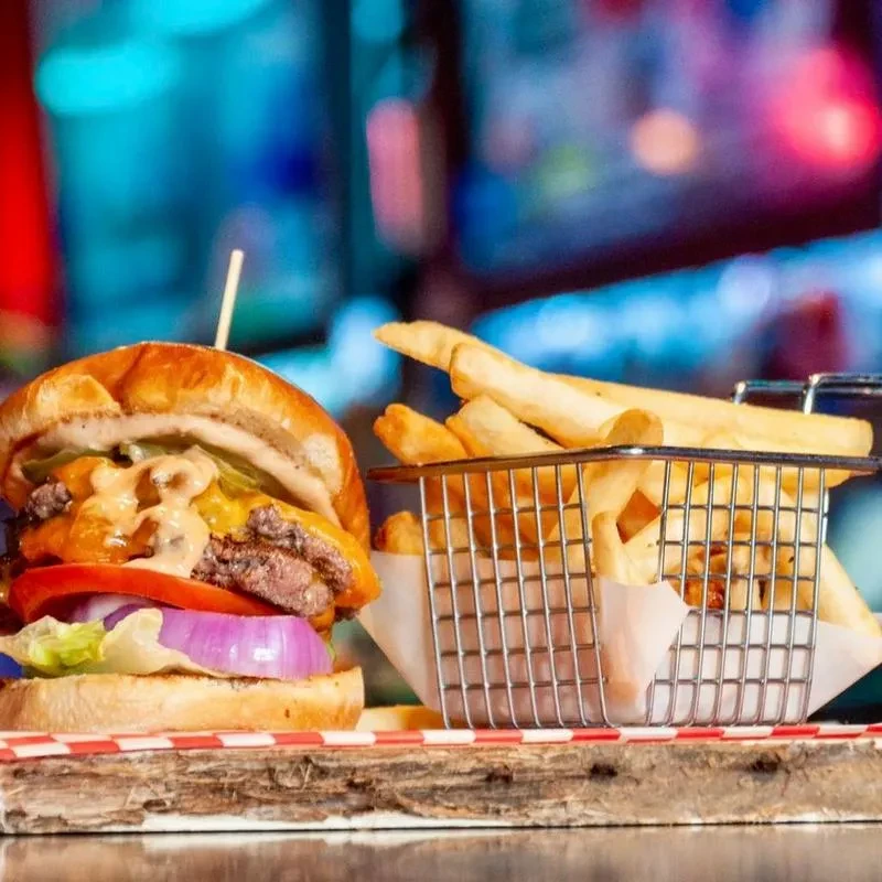 Gourmet cheeseburger, fries, and checkered paper on rustic wooden board.