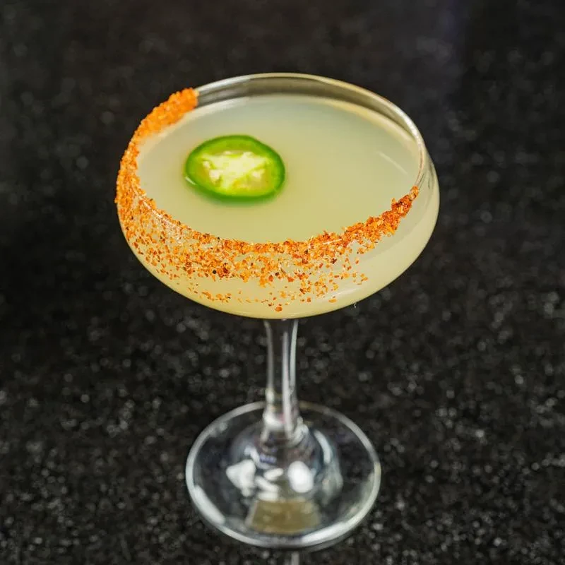 Pale yellow-green cocktail with a spice-rimmed glass and jalapeño slice.