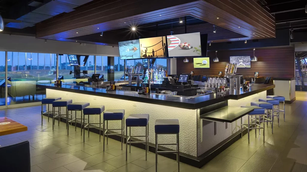 Modern bar interior with sports TVs overlooking a Topgolf range.
