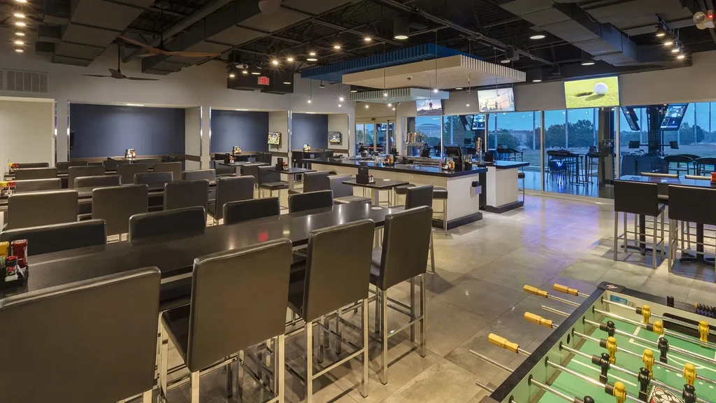 Spacious modern sports bar interior overlooking a golf driving range.