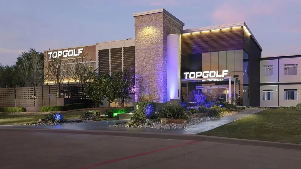Exterior of a modern Topgolf building at dusk with vibrant lighting.