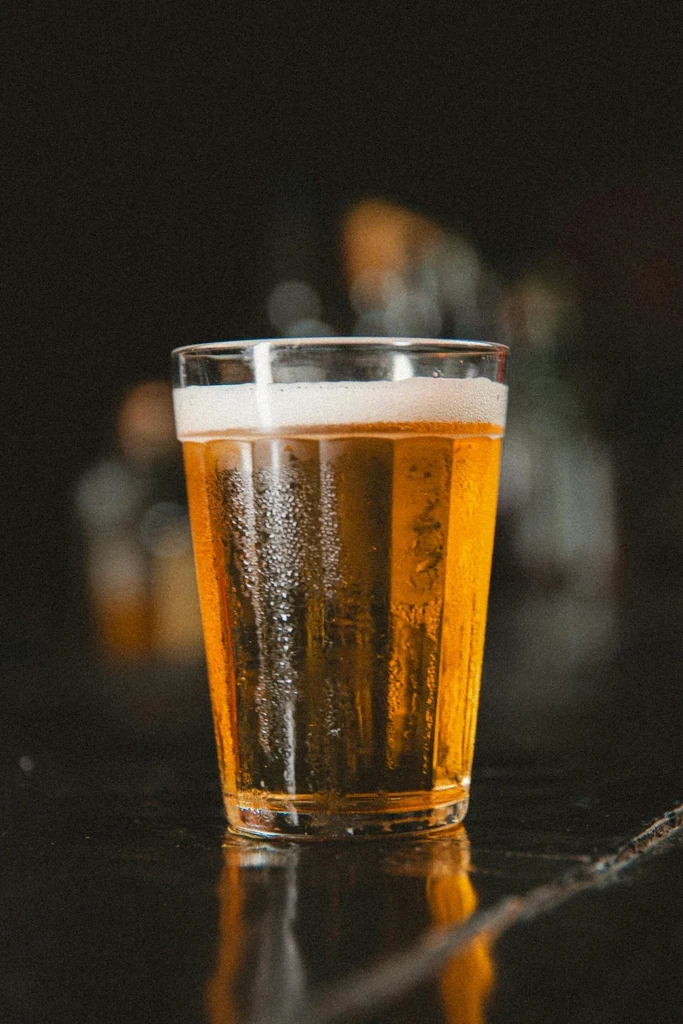 Condensing glass of golden beer with foam on a dark reflective surface.