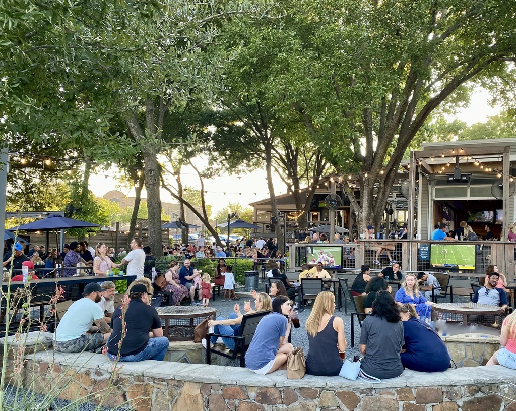 Lively outdoor patio with trees, string lights, and many patrons.