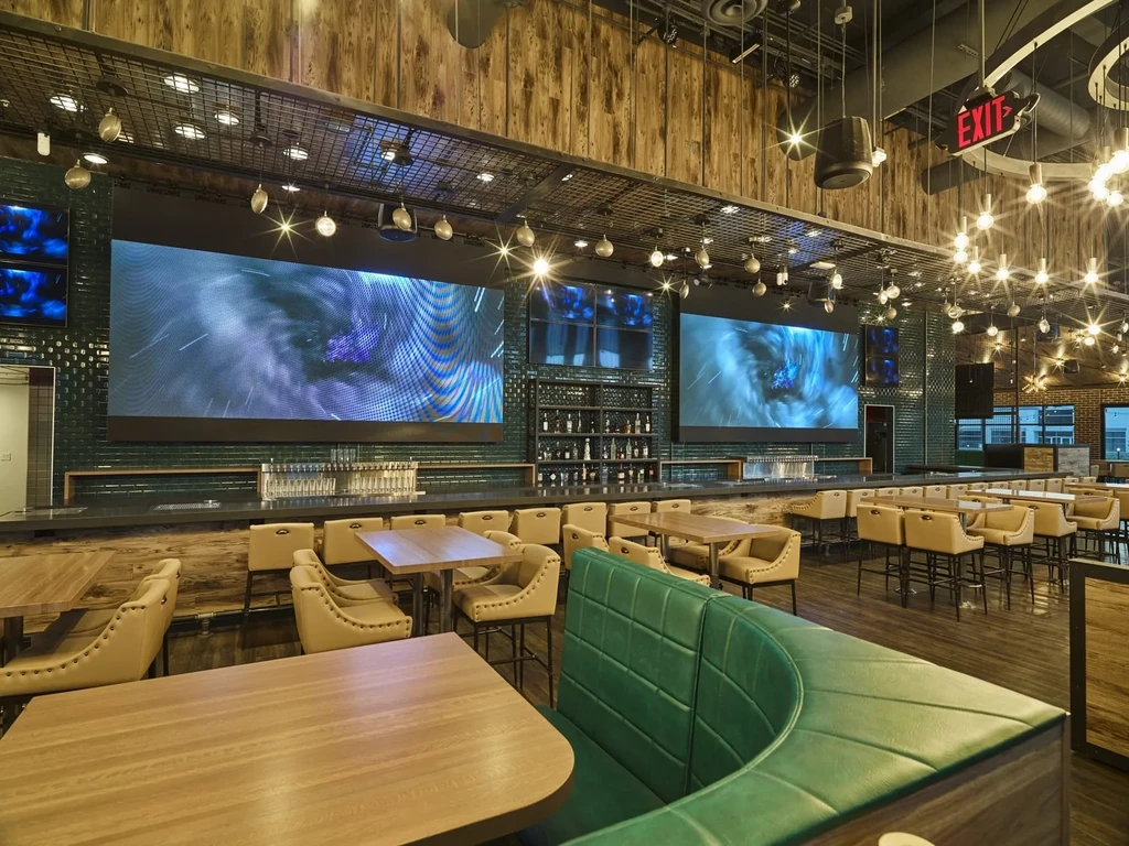 Empty modern bar with green tiled wall, LED screens, and seating.