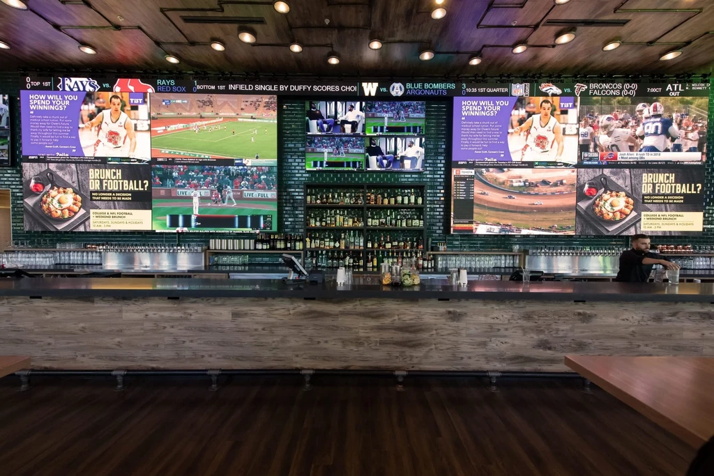 Modern sports bar interior featuring digital screens, beer taps, and a bartender.