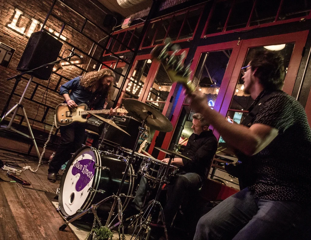 Guitarist, drummer, and bassist perform live in a dimly lit venue.