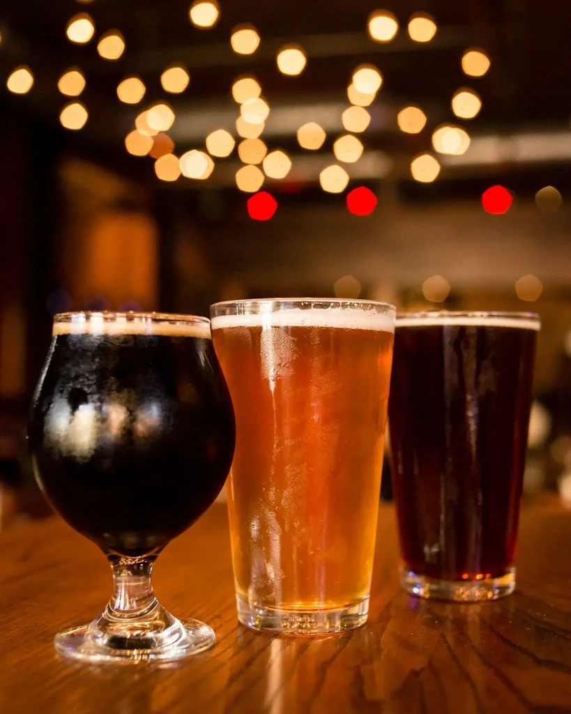 Three distinct cold beers on wood, soft bokeh background.