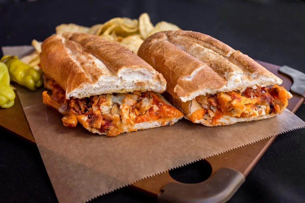 Toasted chicken subs with red sauce and cheese, chips, and peppers.